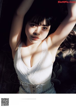 A woman in lingerie sitting on a couch with her hand on her chin.