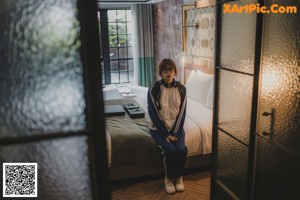 A naked woman sitting on a bed in a hotel room.