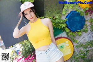 A woman in a yellow top and white shorts posing for a picture.