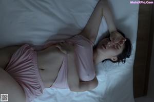 A woman sitting on a bed wearing a pink tank top.