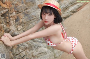 A woman in a bikini and a straw hat on the beach.