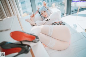 A woman in a white dress and red high heels posing on a white couch.