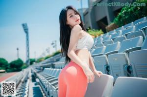 A woman in a white top and orange leggings sitting on a bench.