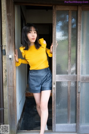 A woman in a yellow sweater sitting on a window sill.