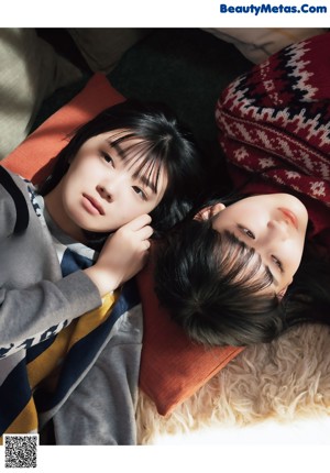 A couple of young women sitting next to each other on a bed.