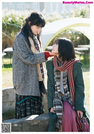 Two young women standing next to each other in front of a tree.
