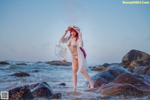 A woman in a bikini and hat sitting on a beach.