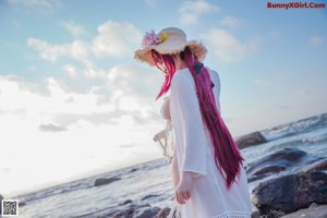 A woman in a bikini and hat sitting on the beach.