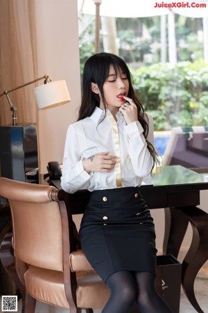 A woman in a white shirt and black skirt sitting on a couch.