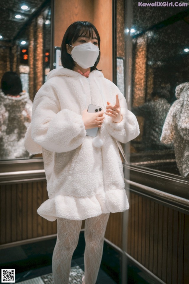 A woman wearing a white coat and a face mask.