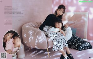 A woman sitting on a pink couch next to a white chair.