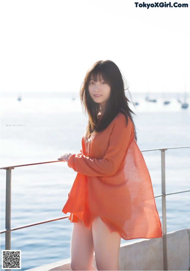 A woman in an orange dress standing by the water.