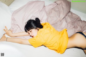 A woman sitting on a bed wearing a yellow shirt.