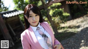 A woman in a pink blazer and tie sitting on a bench.