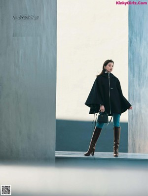 A woman in a black coat standing in front of a window.