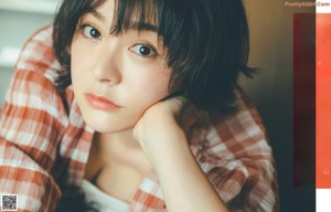 A woman with short black hair wearing a red and white checkered shirt.