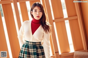 A woman in a white sweater and green plaid skirt posing for a picture.