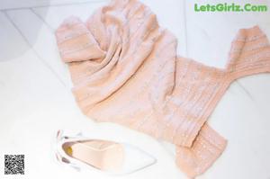 A woman in a pink dress holding up a sweater.
