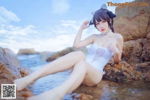 A woman in a white bathing suit sitting on a rock in the water.