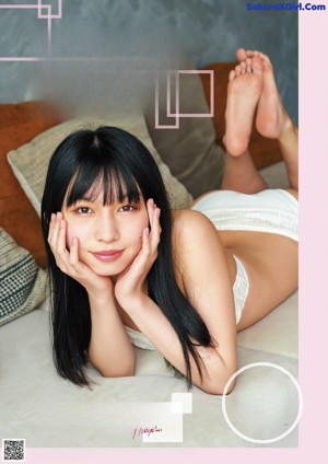 A woman with long black hair sitting on a bed.
