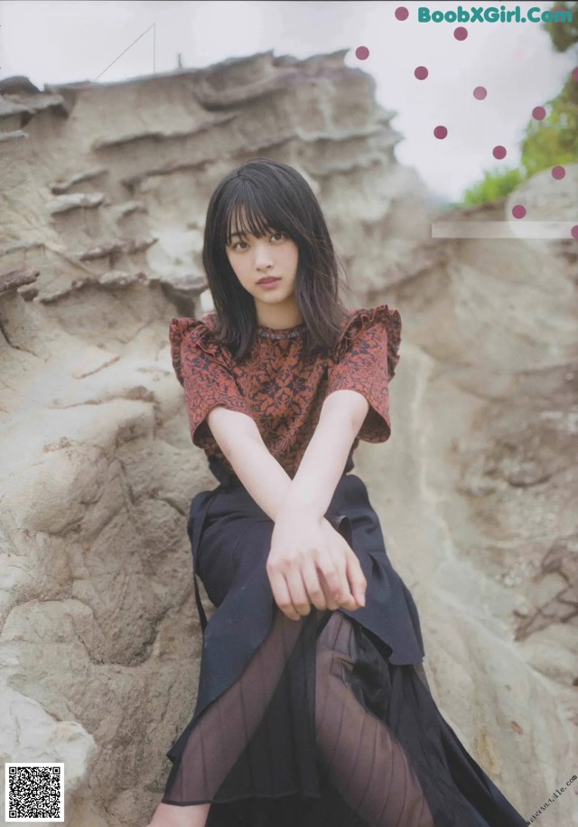 A woman sitting on top of a rock next to a rock wall.